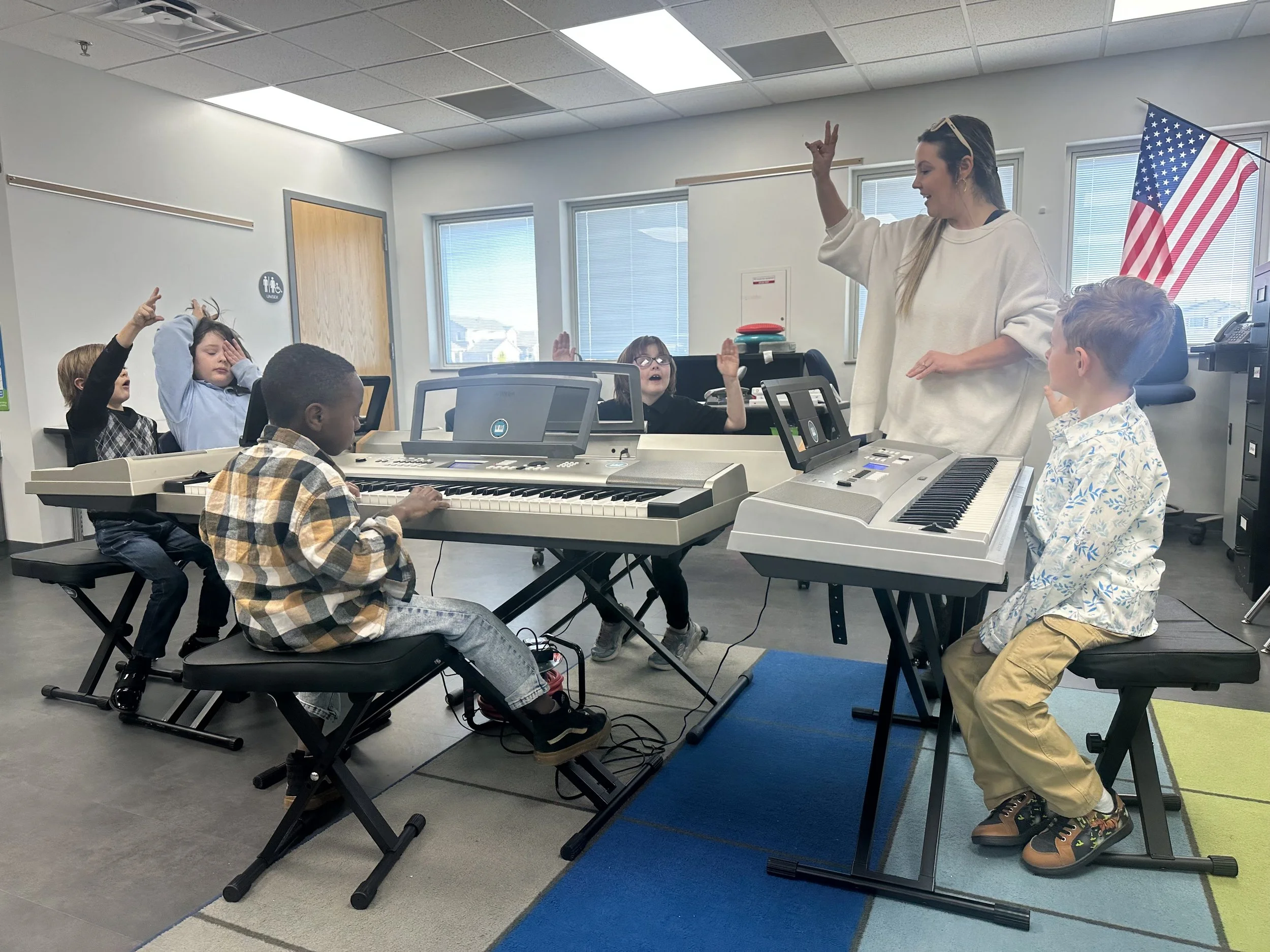 Children participating in an interactive group piano class with a music teacher and digital keyboards.