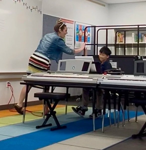 Music teacher encouraging a piano student with a high five during class.