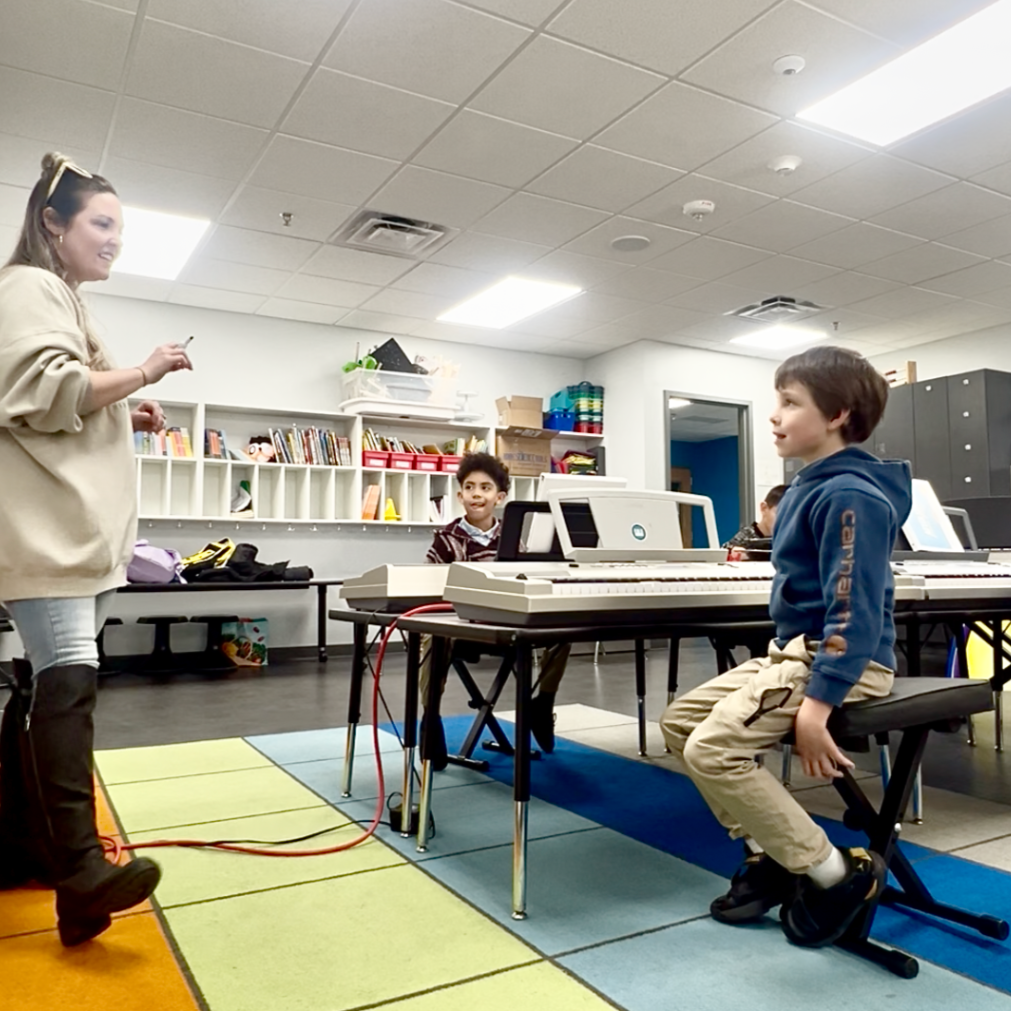 Music teacher leading students during an interactive group piano lesson with digital keyboards.