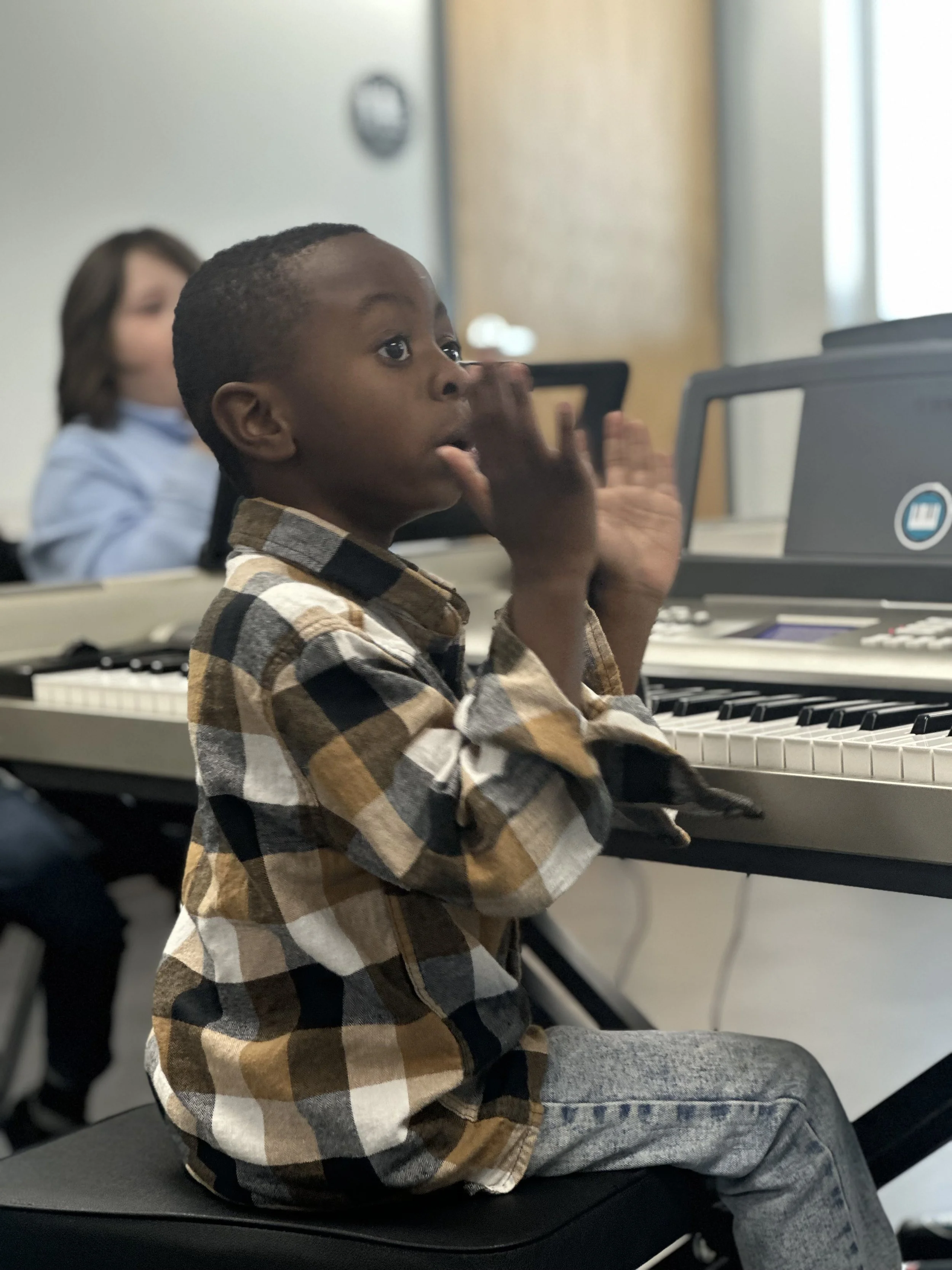 Young student participating in a beginner piano class with a music teacher nearby.