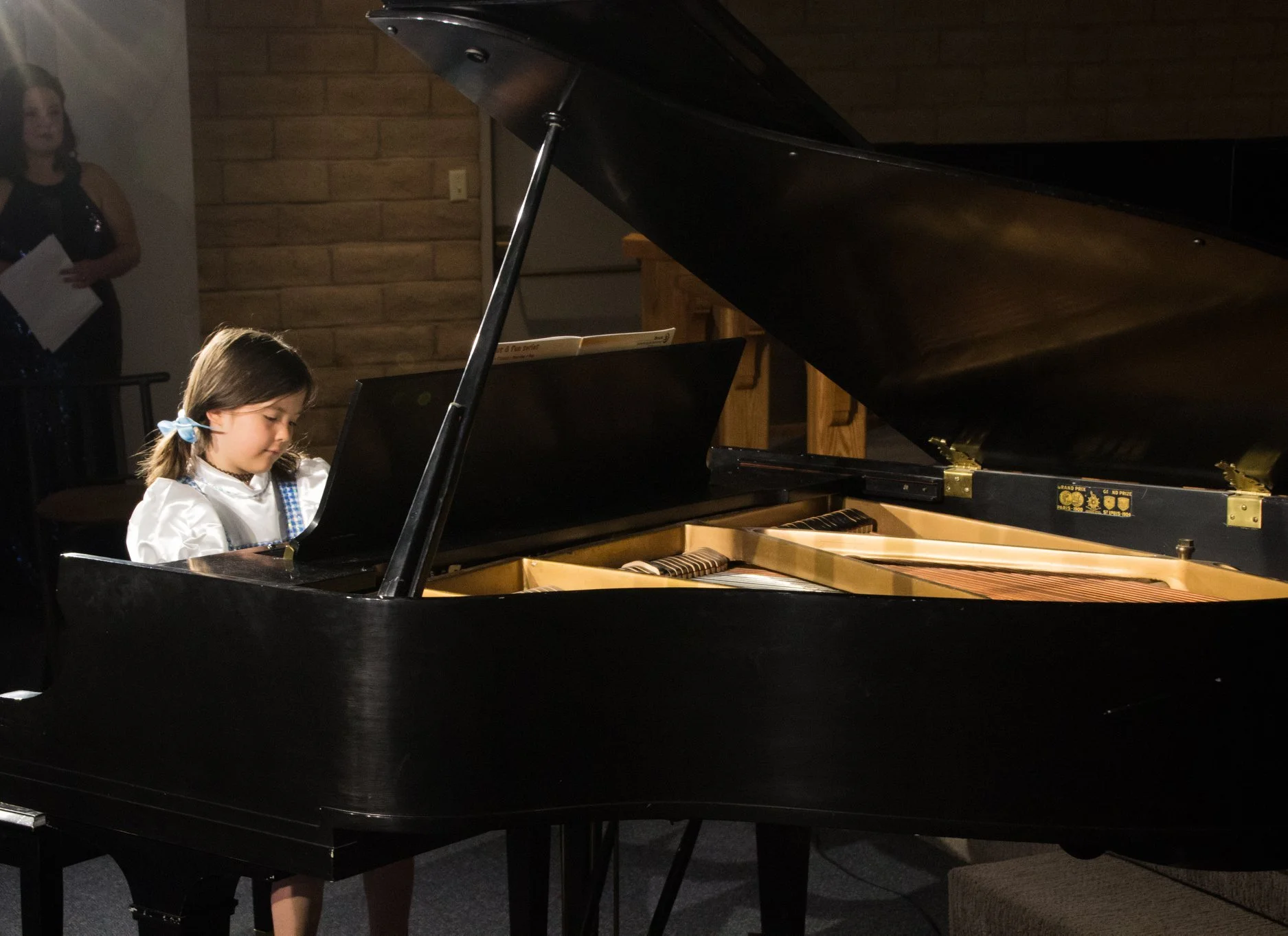 Young piano student performing on a grand piano during a student performance recital.