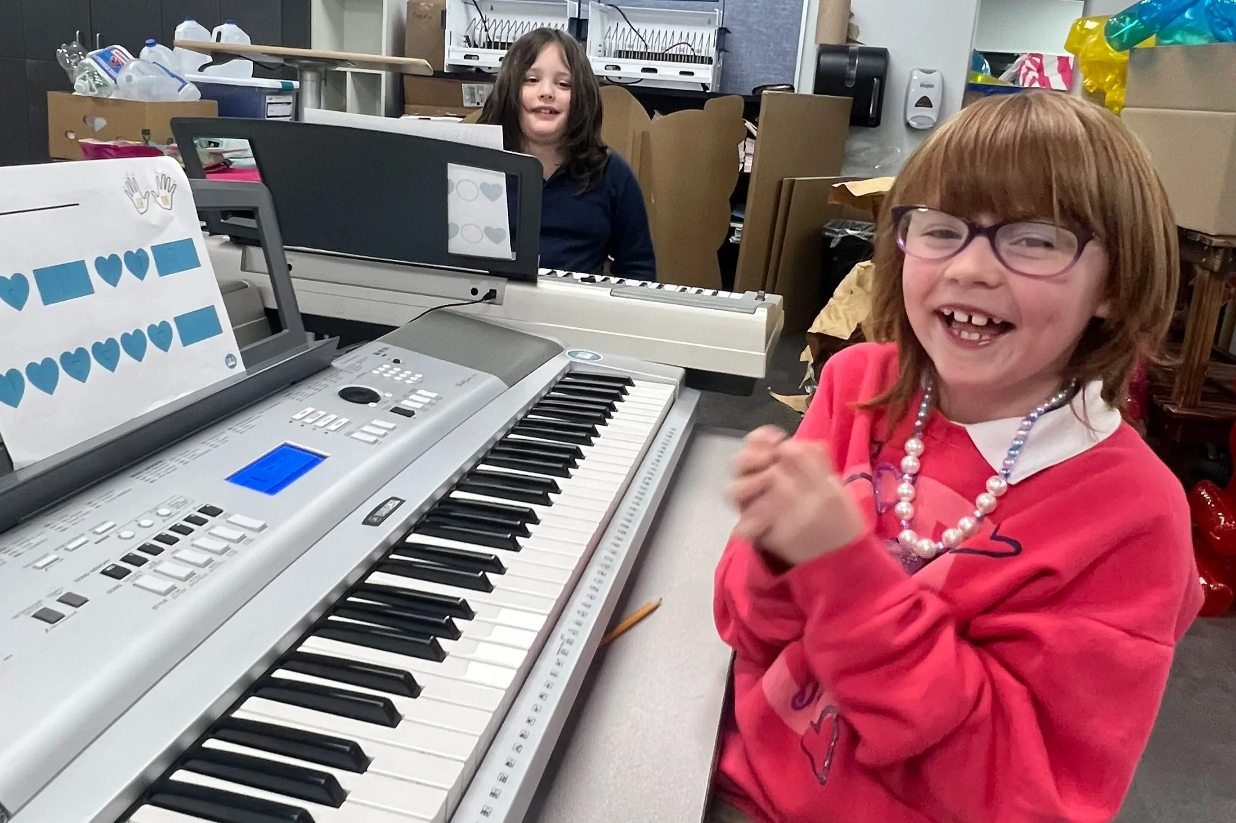 Children smiling during a fun piano lesson in a keyboard classroom.