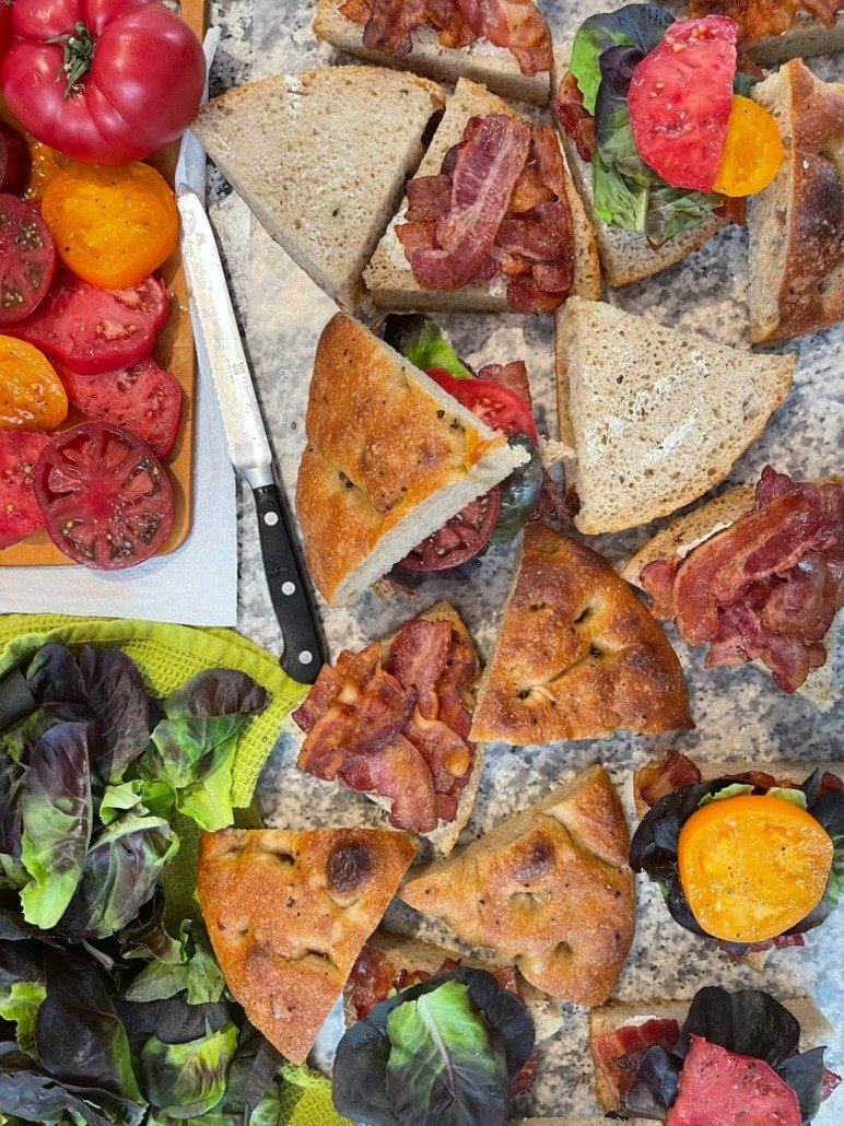 Sliced pizza with bacon, tomato, and greens, mixed with whole tomato varieties on a textured surface.