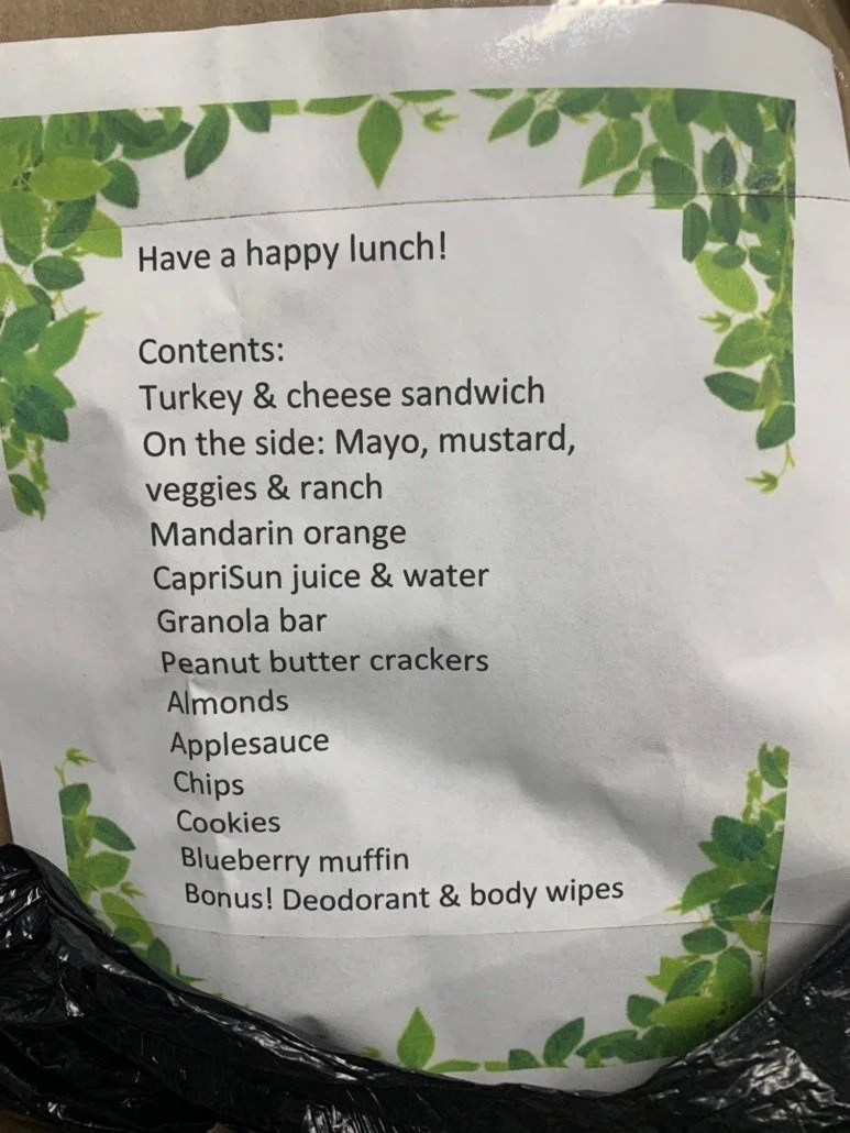 A lunch menu with a green leafy border, listing contents including a turkey and cheese sandwich, side of mayo, mustard, veggies, ranch, mandarin orange, CapriSun juice and water, granola bar, peanut butter crackers, almonds, applesauce, chips, cookie