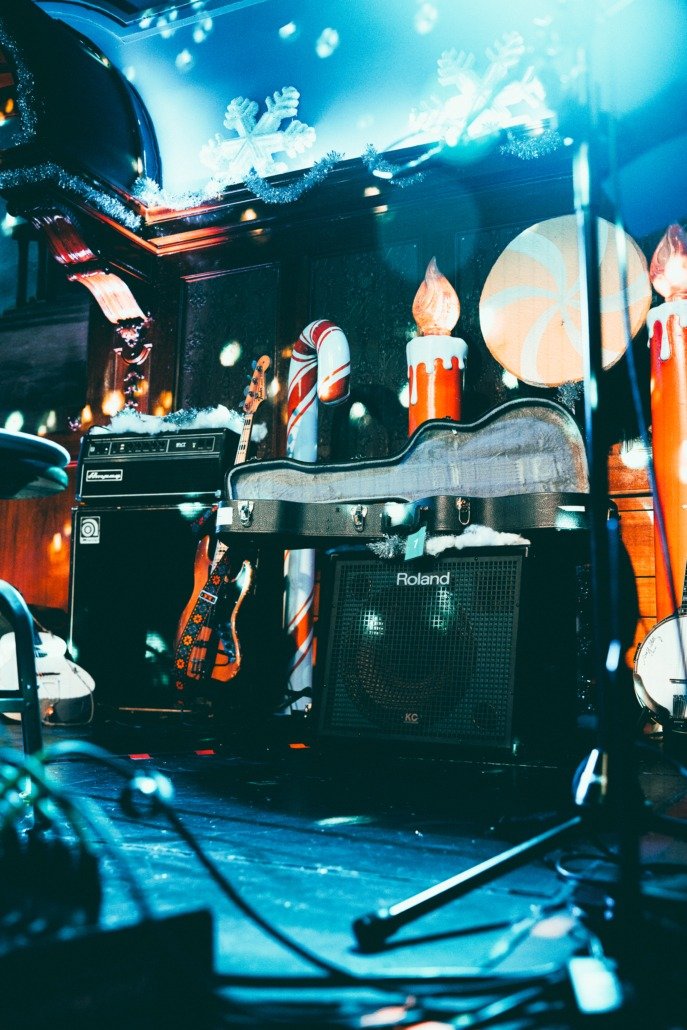 Stage decorated with Christmas lights and ornaments, featuring a guitar, an amplifier, and musical equipment.