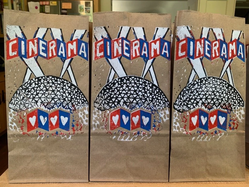 Decorative paper bags with 'CINERAMA' written on top, designed with a black and white geometric pattern umbrella, and red, white, and blue hearts and blocks underneath.