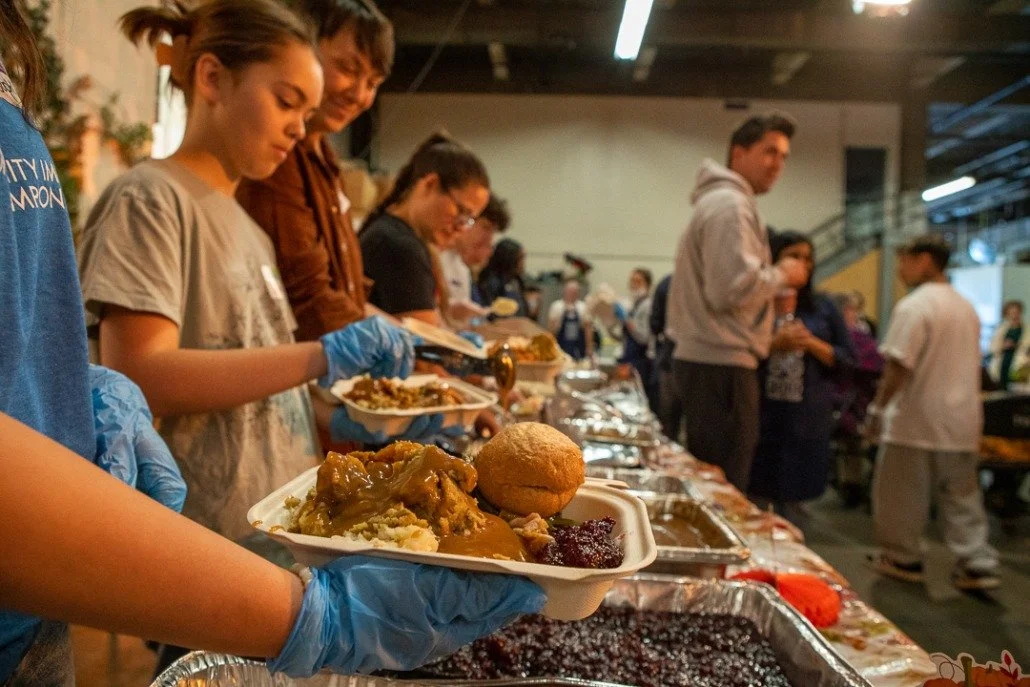 People serving themselves food from a buffet table at a community meal event.