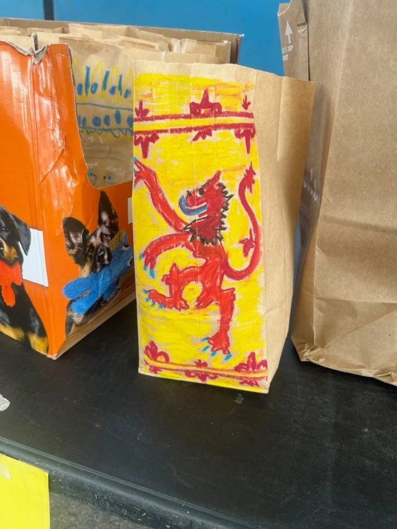 A hand-drawn picture of a red lion with a yellow background, outlined in red, with some blue details, on a brown paper bag.