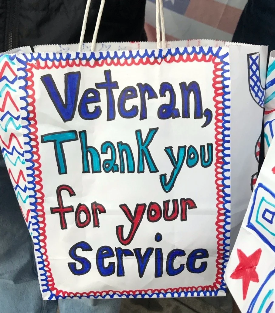 Colorful handmade sign with red, blue, and black text that reads, 'Veteran, Thank you for your service,' decorated with patriotic colors and patterns.