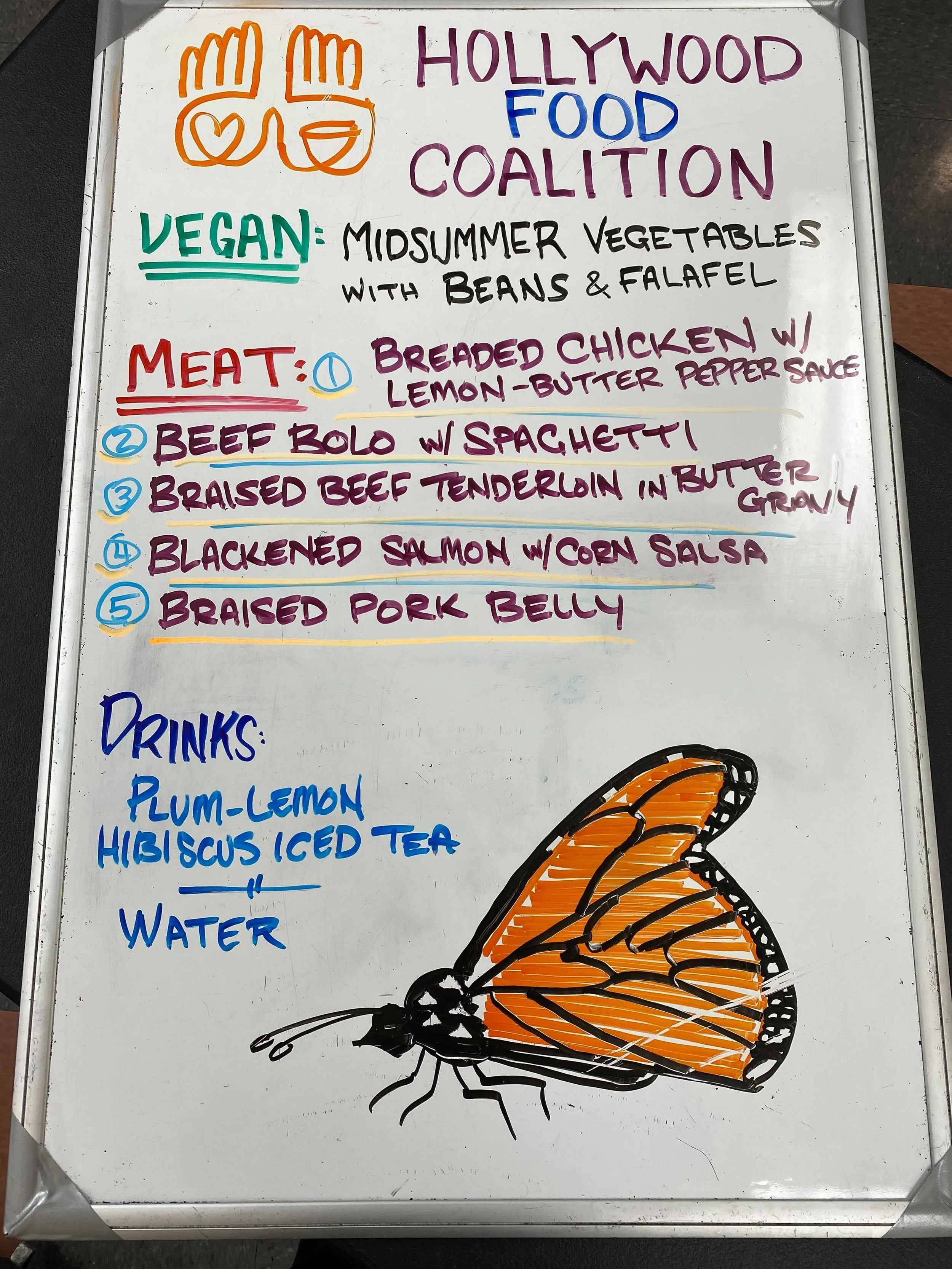 Whiteboard menu for Hollywood Food Coalition with sections for vegan, meat dishes, and drinks, featuring drawings of an orange butterfly and colorful text.