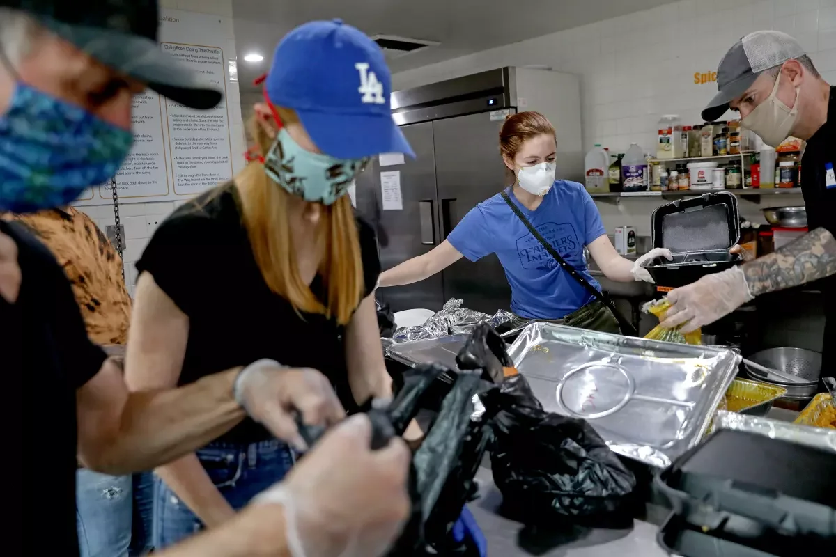 People working in a commercial kitchen, preparing and packaging food while wearing face masks and gloves.