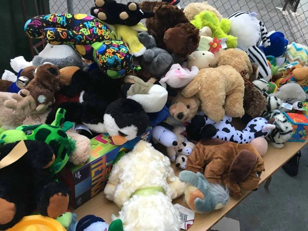 Table full of assorted plush toys, including animals, monsters, and birthday-themed stuffed animals.