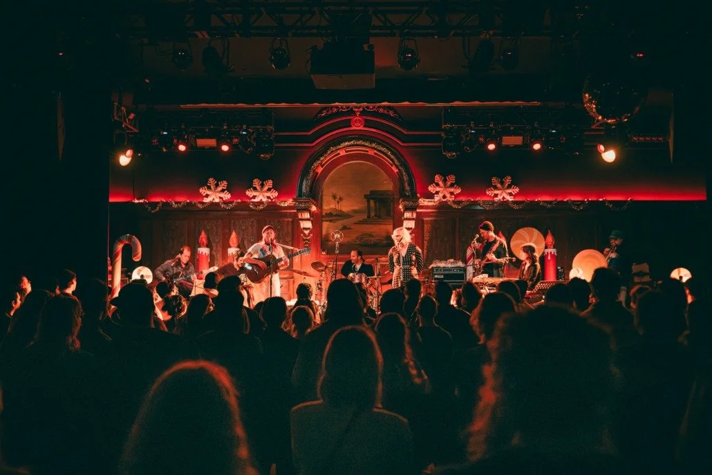A live musical performance on stage with Christmas decorations, including snowflakes and candles, and an audience watching.