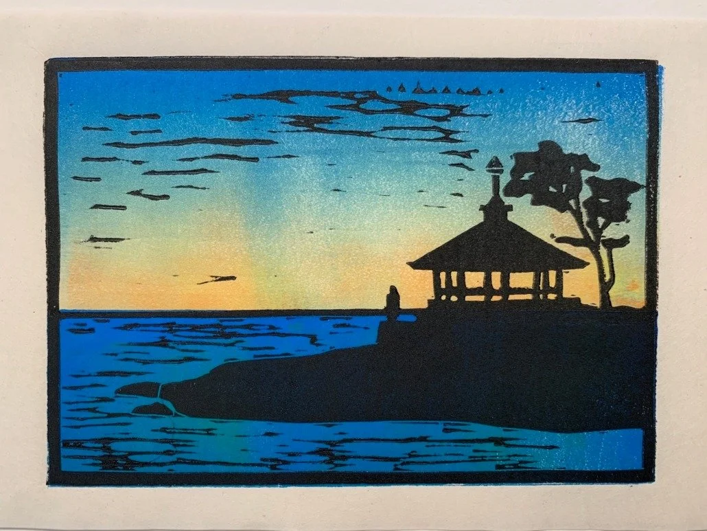 Silhouette of a person walking near a gazebo on a coastline during sunset, with a tree nearby and a colorful sky reflected on the water.