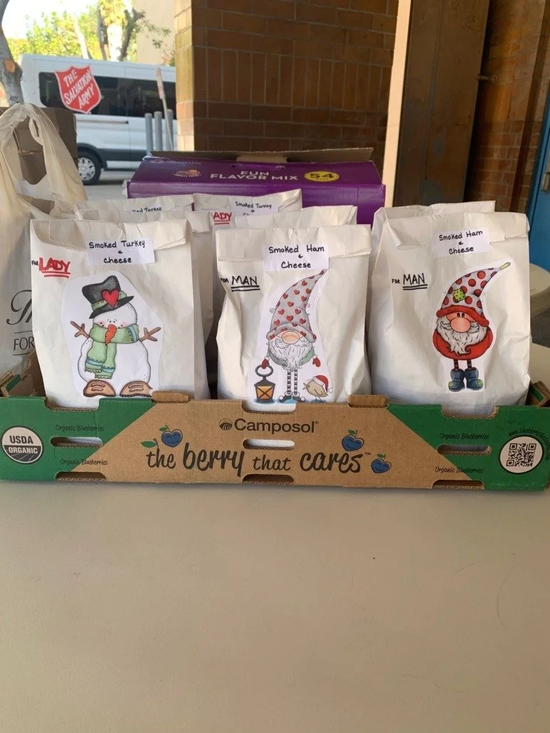 Packaged smoked turkey and smoked ham cheese in gift bags with Christmas gnome and snowman illustrations displayed in a cardboard box with blueberry branding.