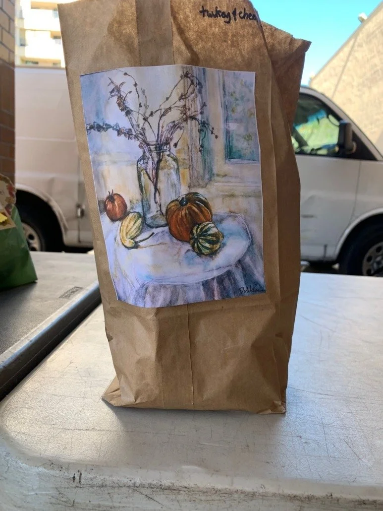 Browning paper bag with a still-life watercolor painting of pumpkins, a gourd, and a glass jar with dried plants on a table near a window.