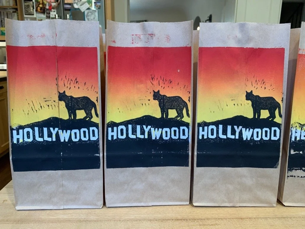 Paper bags with a silhouette of a mountain lion and the word 'Hollywood' against a sunset background.