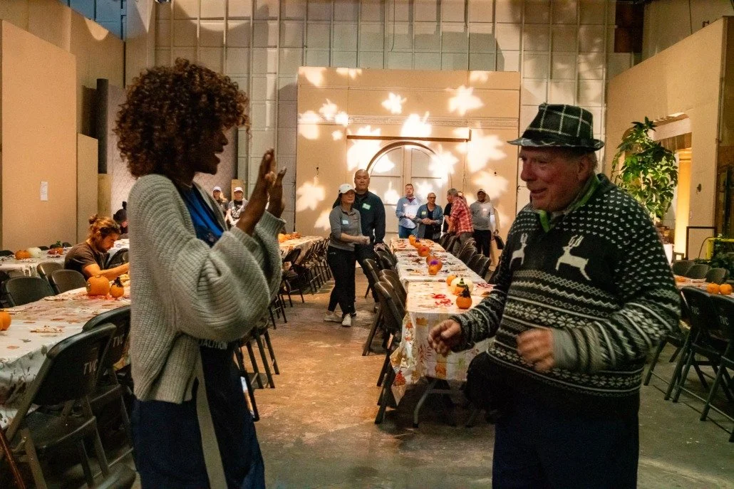 Two people happily conversing in a decorated indoor space with long tables, pumpkins, and fall-themed decor.