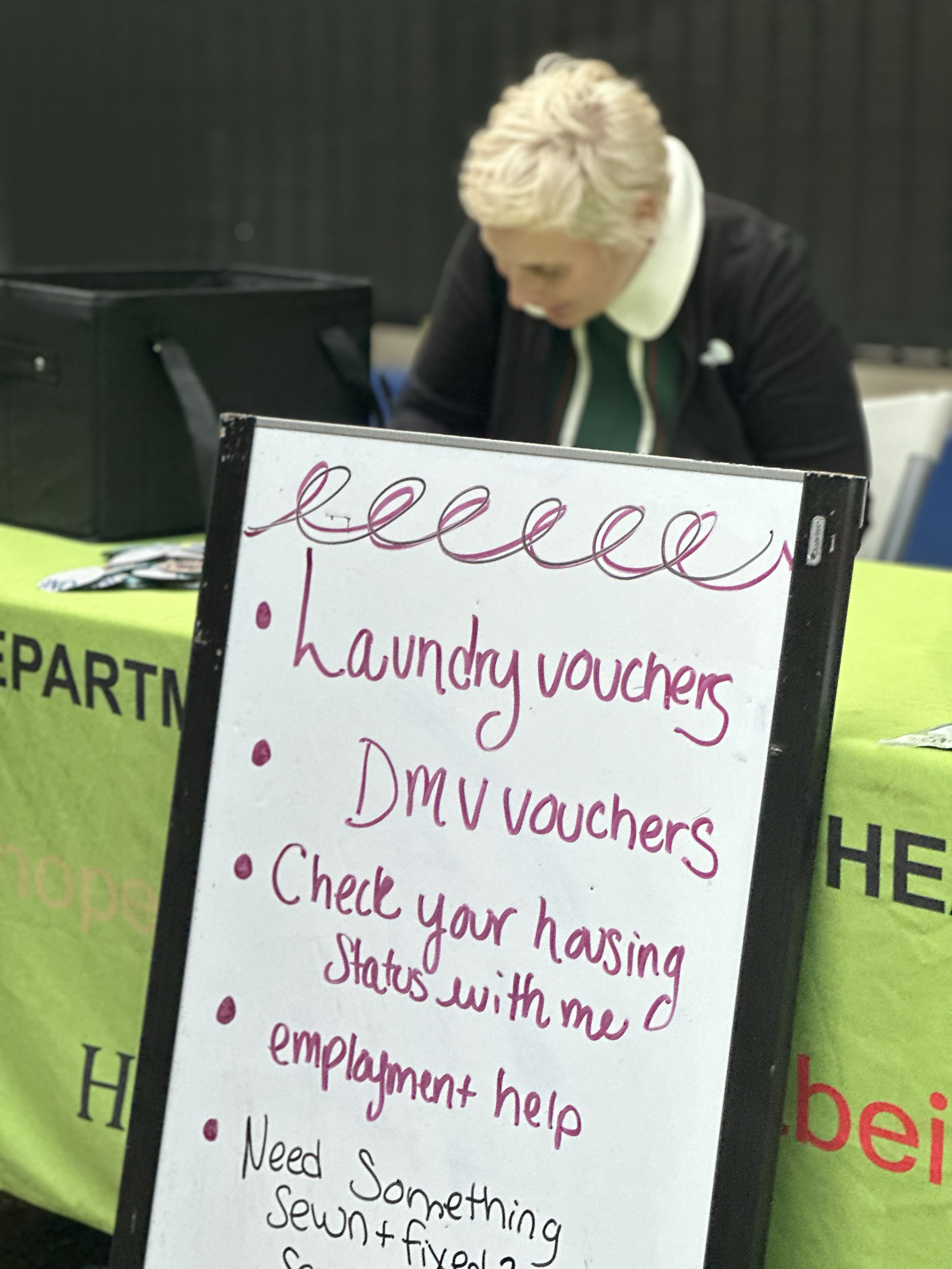 A woman at a booth with a sign offering laundry vouchers, DMV vouchers, and employment help.