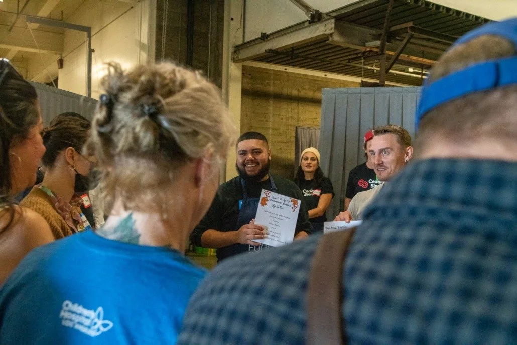 A group of people gathered indoors, with one individual holding a certificate, smiling, while others look on.