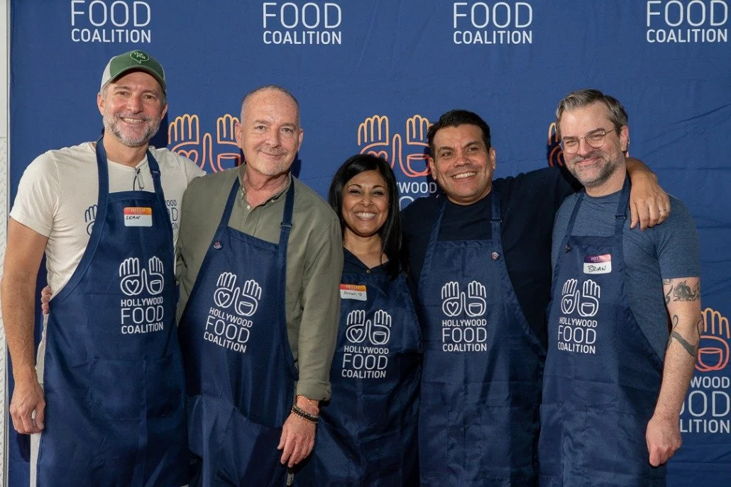 Five people standing together at a Food Coalition event, wearing aprons with the Food Coalition logo, smiling for the camera.