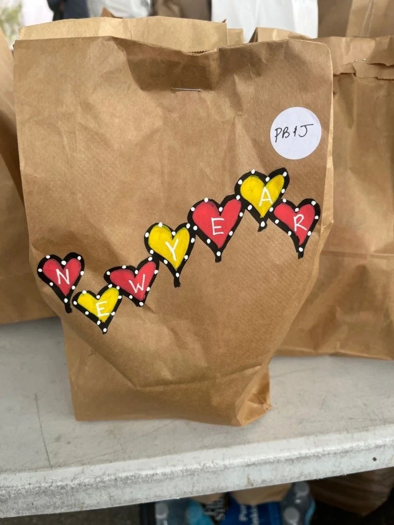 Brown paper bag decorated with colorful heart-shaped cutouts spelling "NEW YEAR" on a white surface.