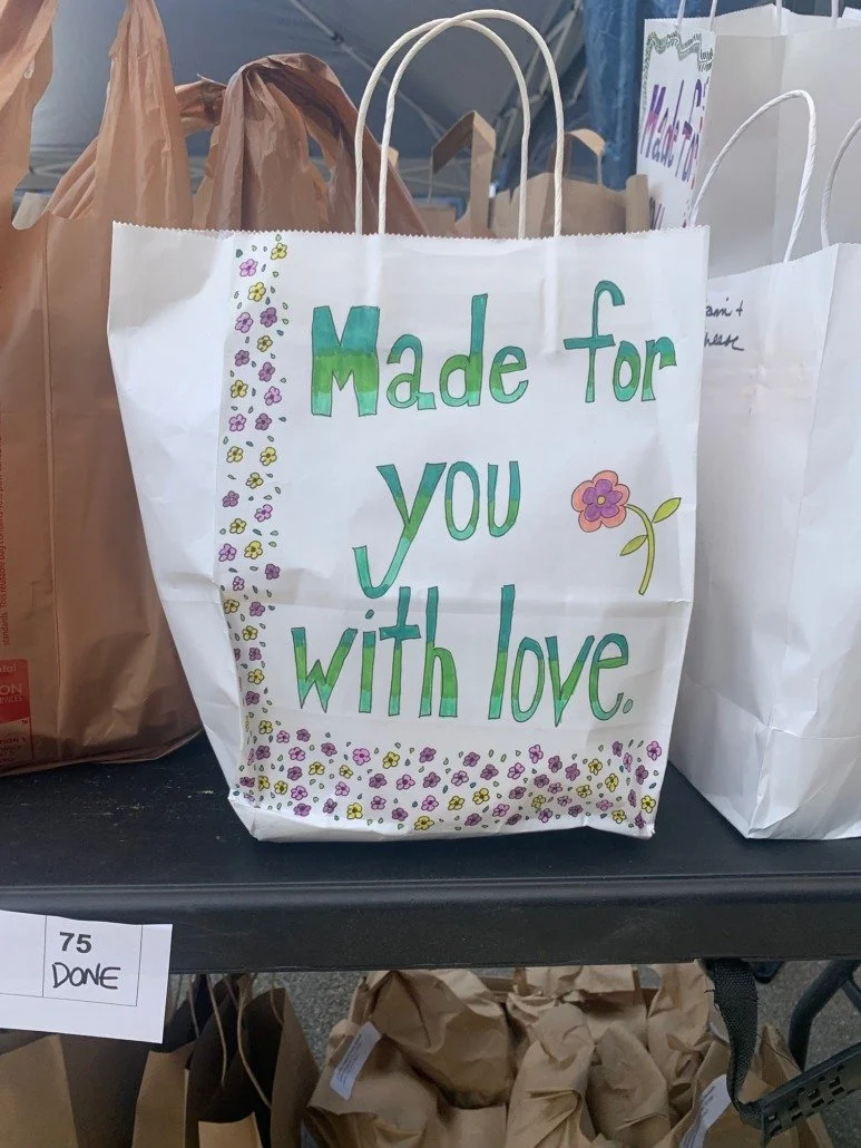 White paper gift bag with colorful hand-drawn message: 'Made for you with love', decorated with flowers and a small pink and purple flower drawing.