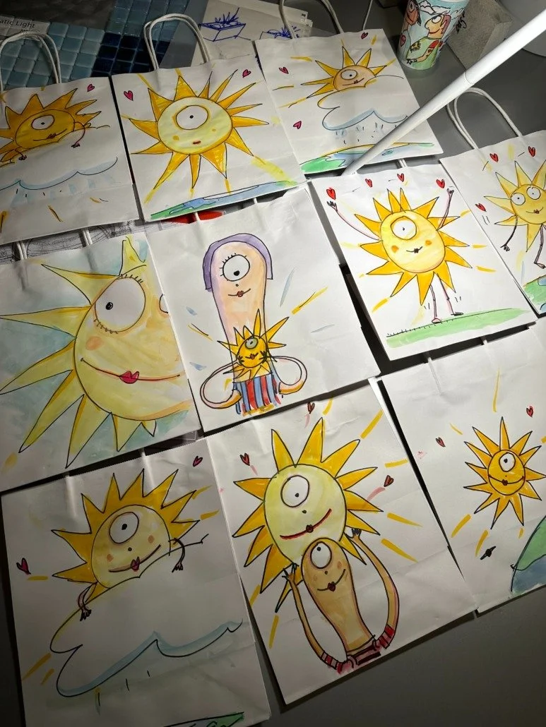 Collection of hand-drawn and painted cartoon sun characters, some with one eye and some with two, on paper sheets with colorful backgrounds.