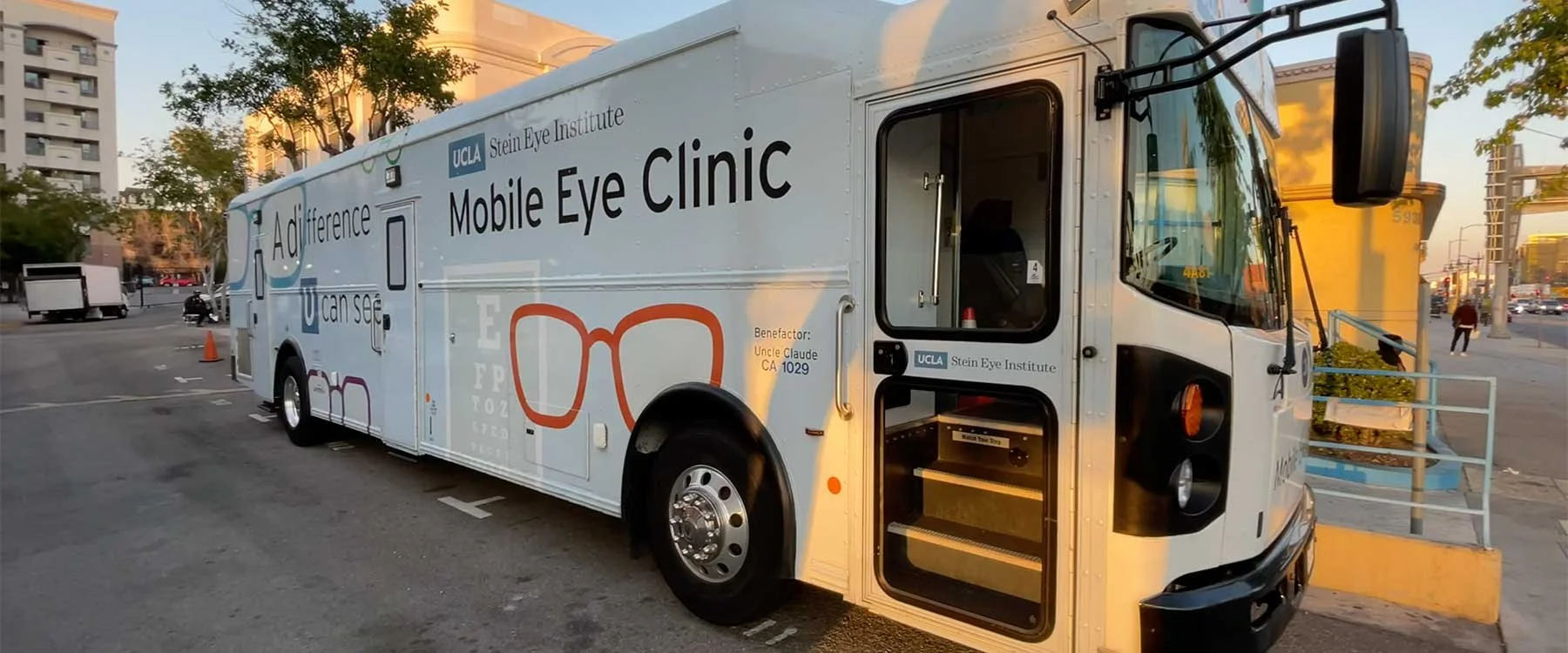 Mobile eye clinic truck with UCLA Stein Eye Institute branding parked on a city street during sunset, surrounded by buildings and trees.