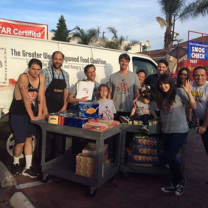 Group of people distributing food and supplies in a parking lot during daytime with palm trees in the background, next to a vehicle with a sign for a food coalition.
