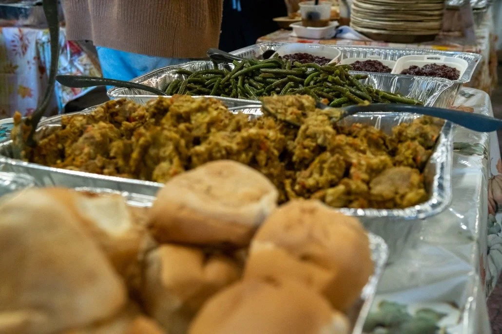 Assorted dishes at a buffet table, including green beans, a mixture of seasoned vegetables, and bread rolls.