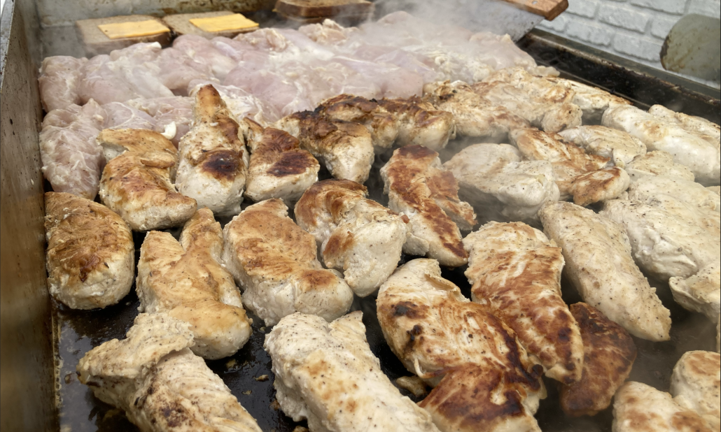 Boneless chicken pieces and chicken drumsticks being grilled on a flat-top grill.