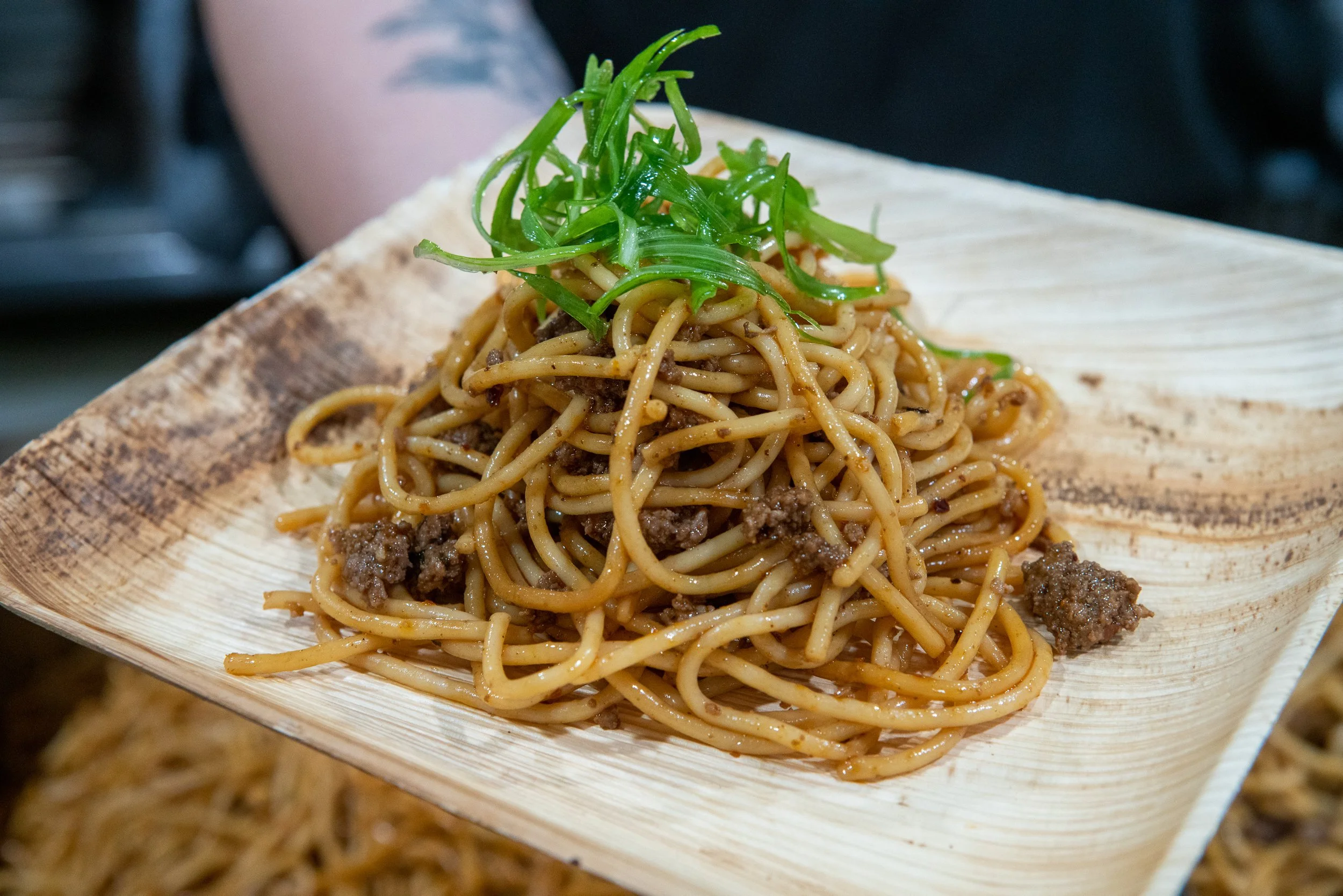 A serving of stir-fried noodles with ground meat and chopped green onions on a wooden plate.