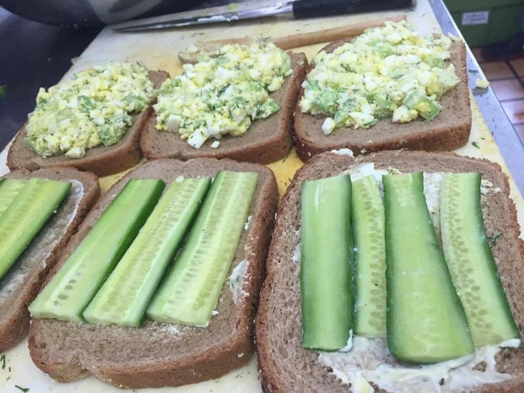 Six slices of bread topped with cucumber slices and egg salad.