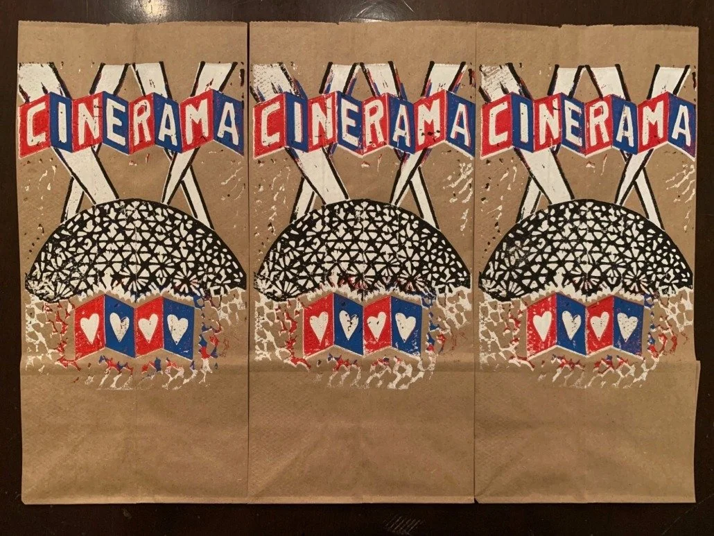 Triptych of paper art featuring the word 'CINERAMA', a stylized black dome, red and blue banners with hearts, and a crowd of small white figures.