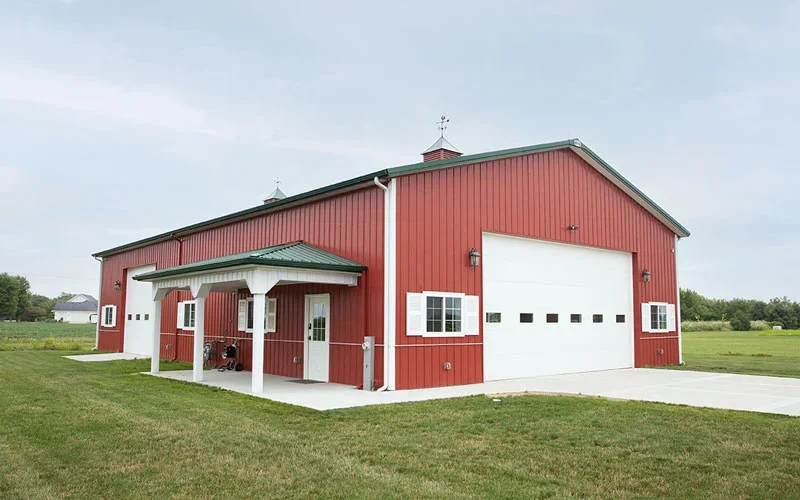 Red barn with white garage door, small porch, and green roof, situated in a grassy field.