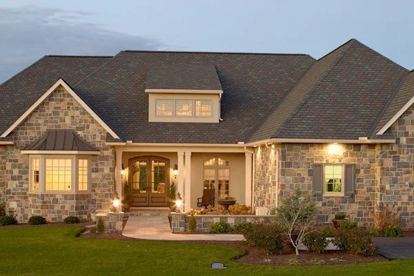 Front view of a large house with stone and siding exterior, front porch, and well-maintained lawn.