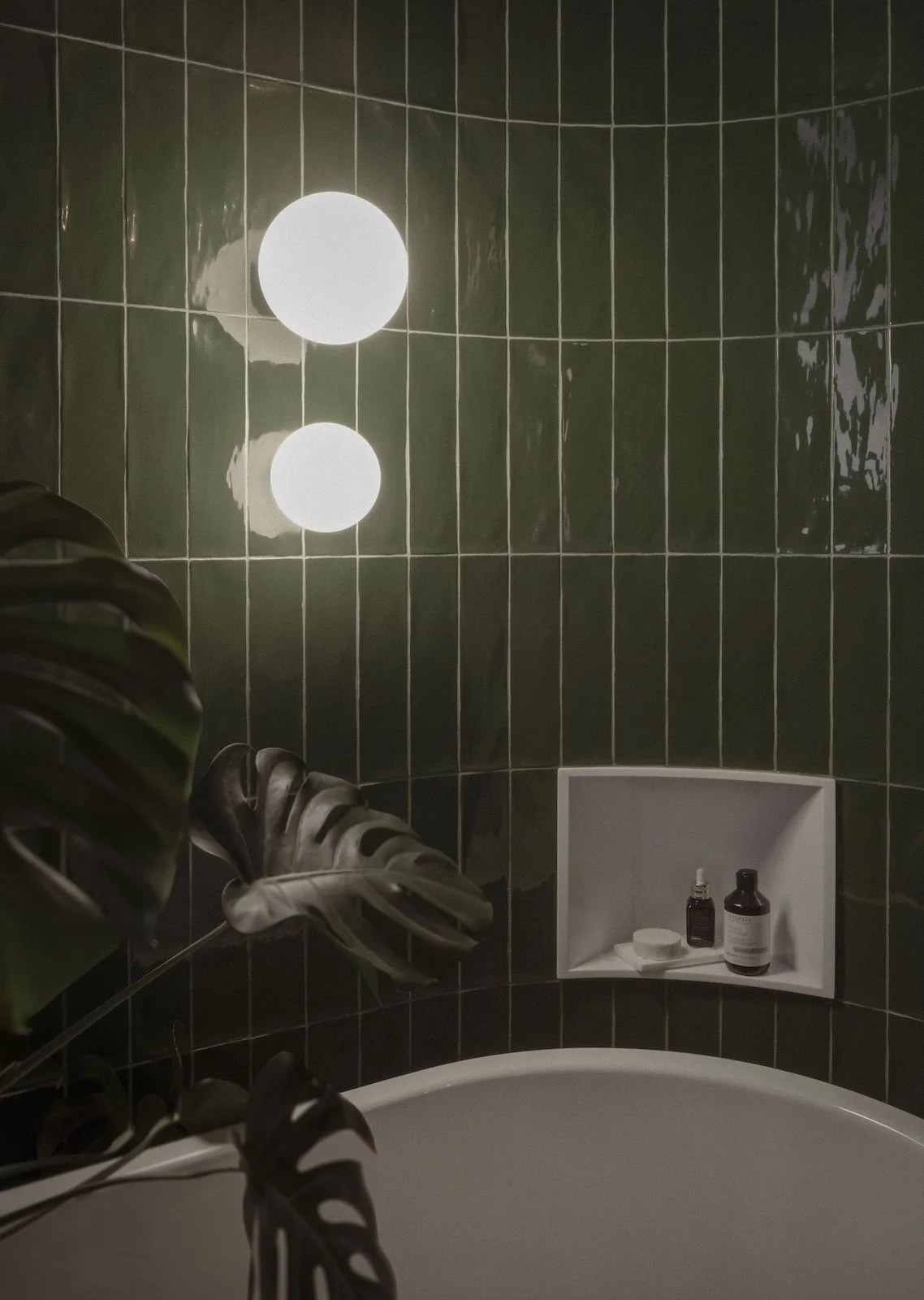 Bathroom interior of Goldfish Apartments by Jenny Ly Studio — deep green glazed tiles, round lighting fixtures, and organic composition.