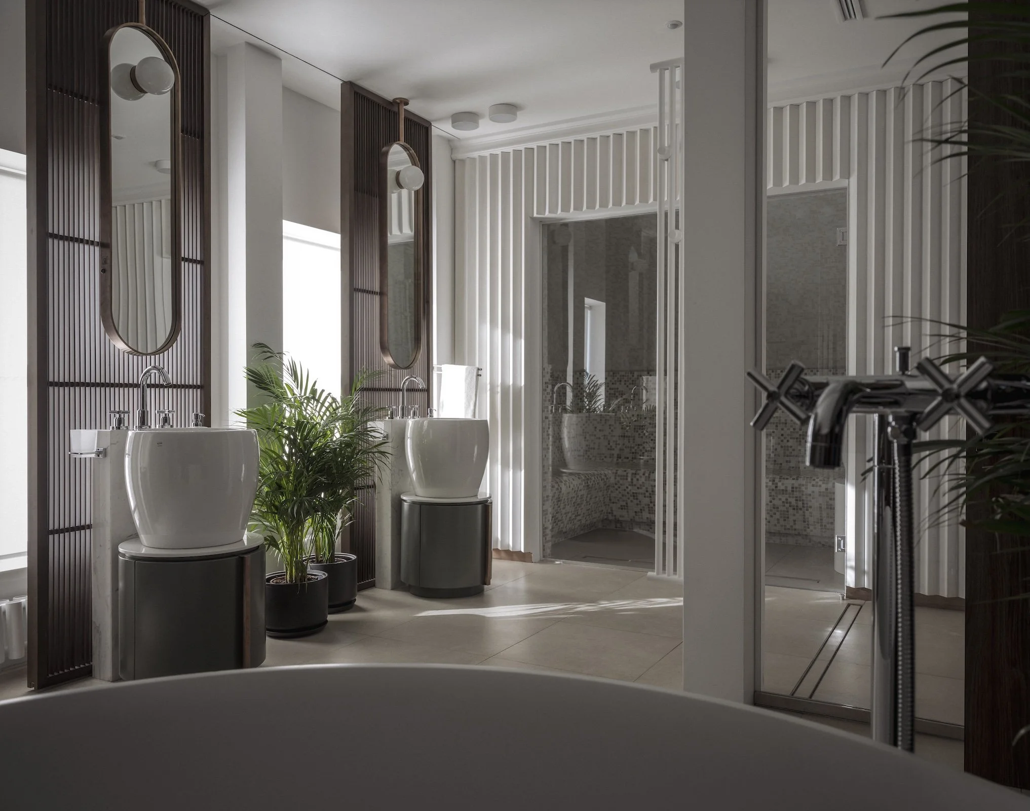 Modern bathroom with two white vessel sinks, decorative wood mirrors, potted plants, a shower with glass enclosure, and a heated towel rack.