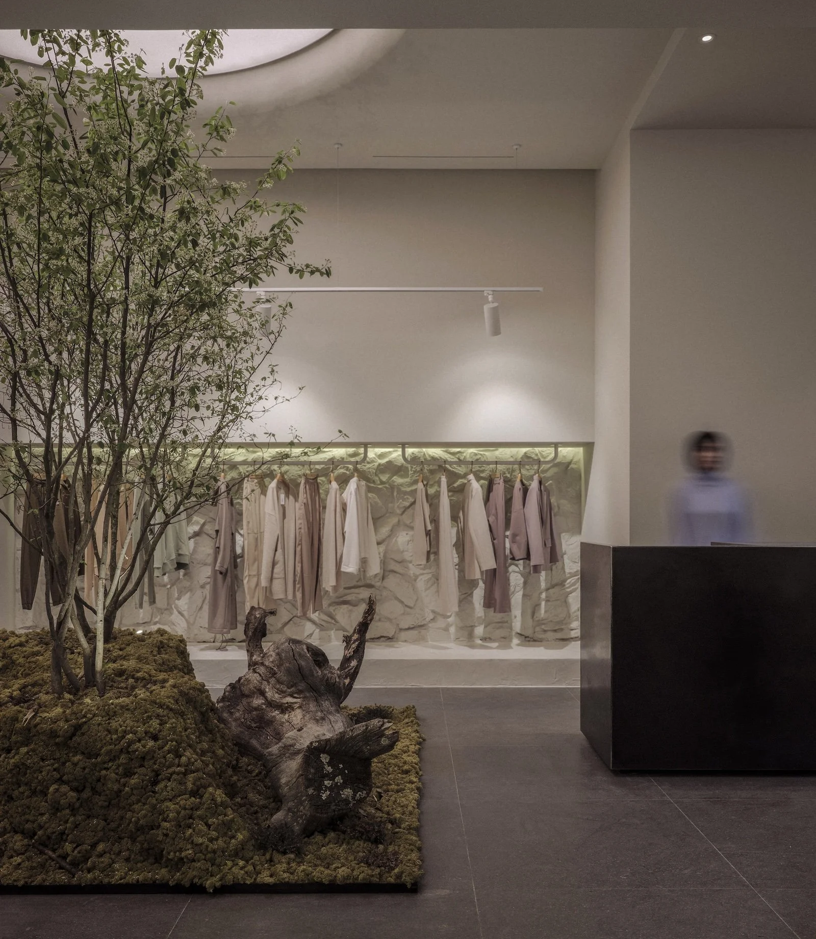 Reception area interior design of Latrika Brand Store by Jenny Ly Studio — natural moss landscape, indoor tree, and stone-textured garment display.