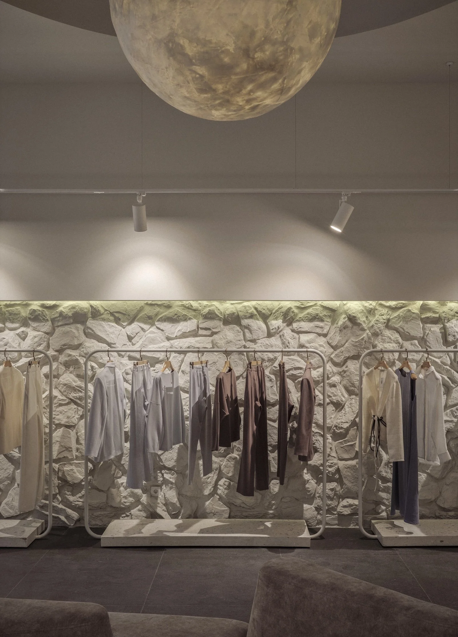 Interior design of Latrika Brand Store by Jenny Ly Studio — textured stone display wall with neutral-toned garments and soft ambient lighting