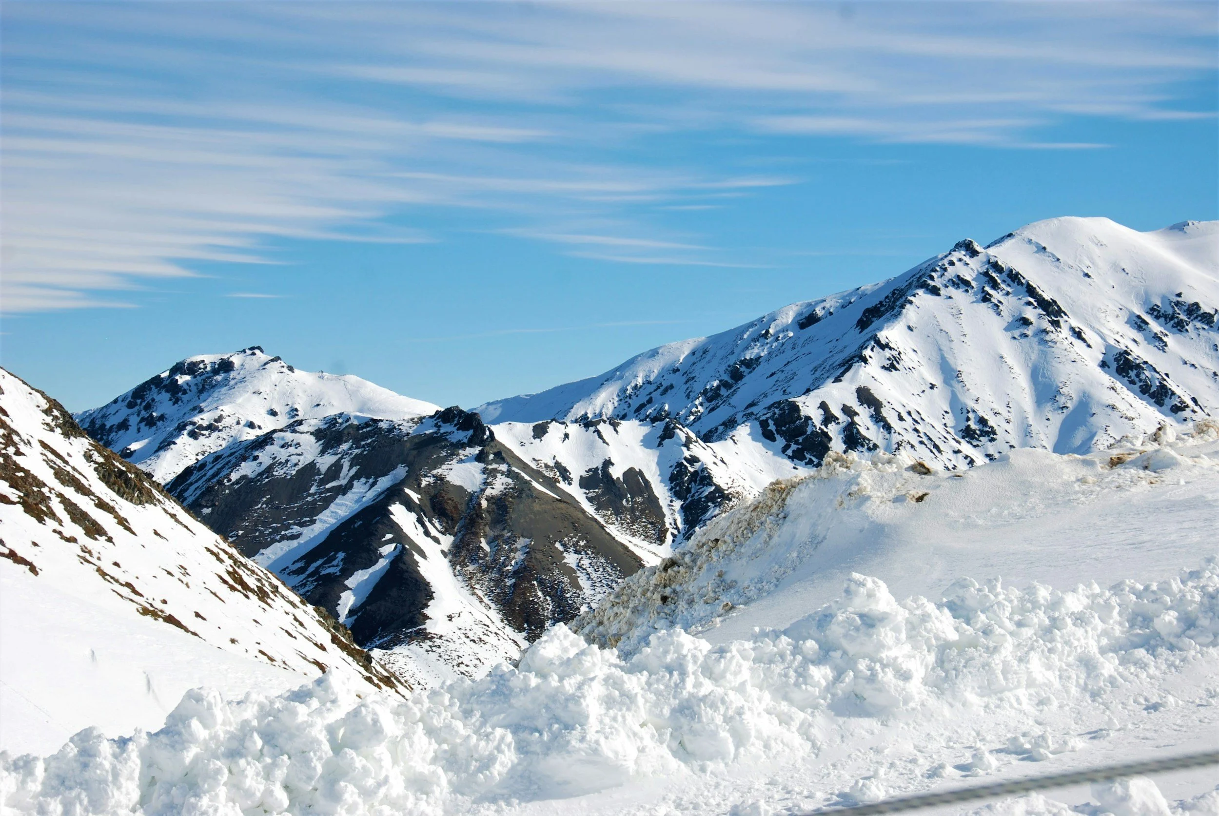Snow-covered mountain peaks in Queenstown, New Zealand, under a clear blue sky with streaks of clouds.