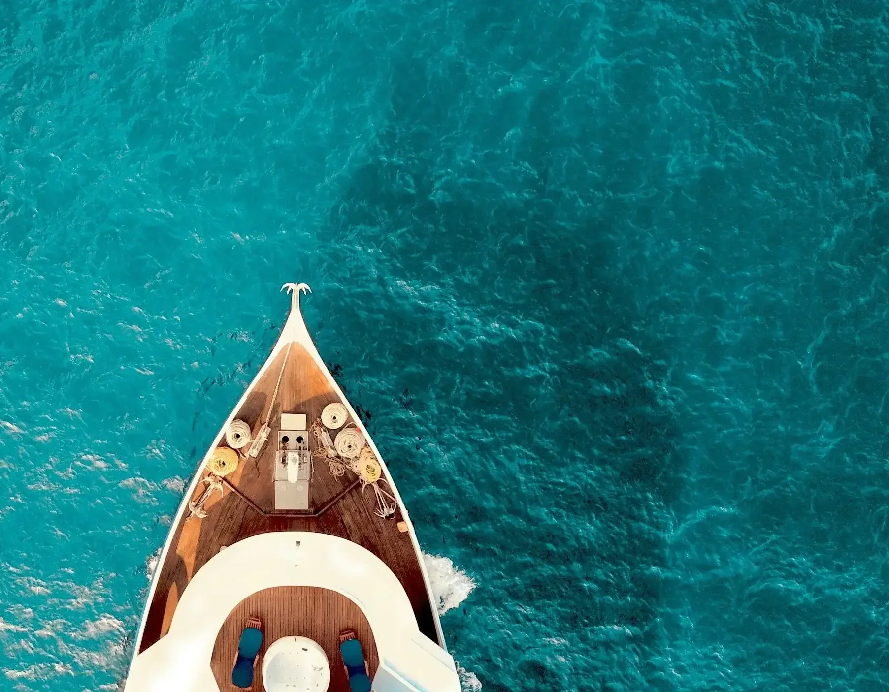 Aerial view of a boat with a wooden deck navigating through blue ocean water.
