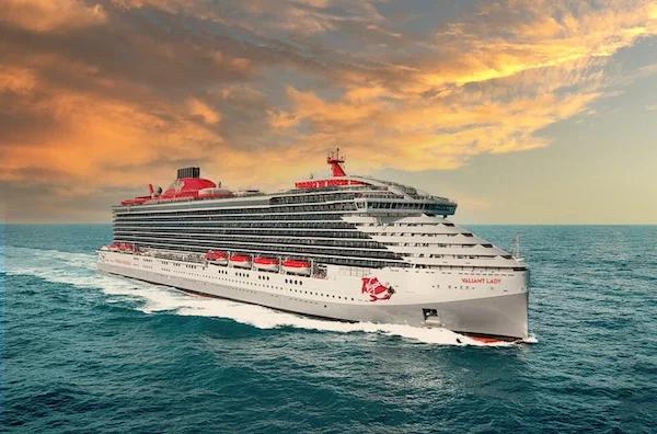Large white cruise ship on the ocean during sunset with orange and yellow clouds in the sky.