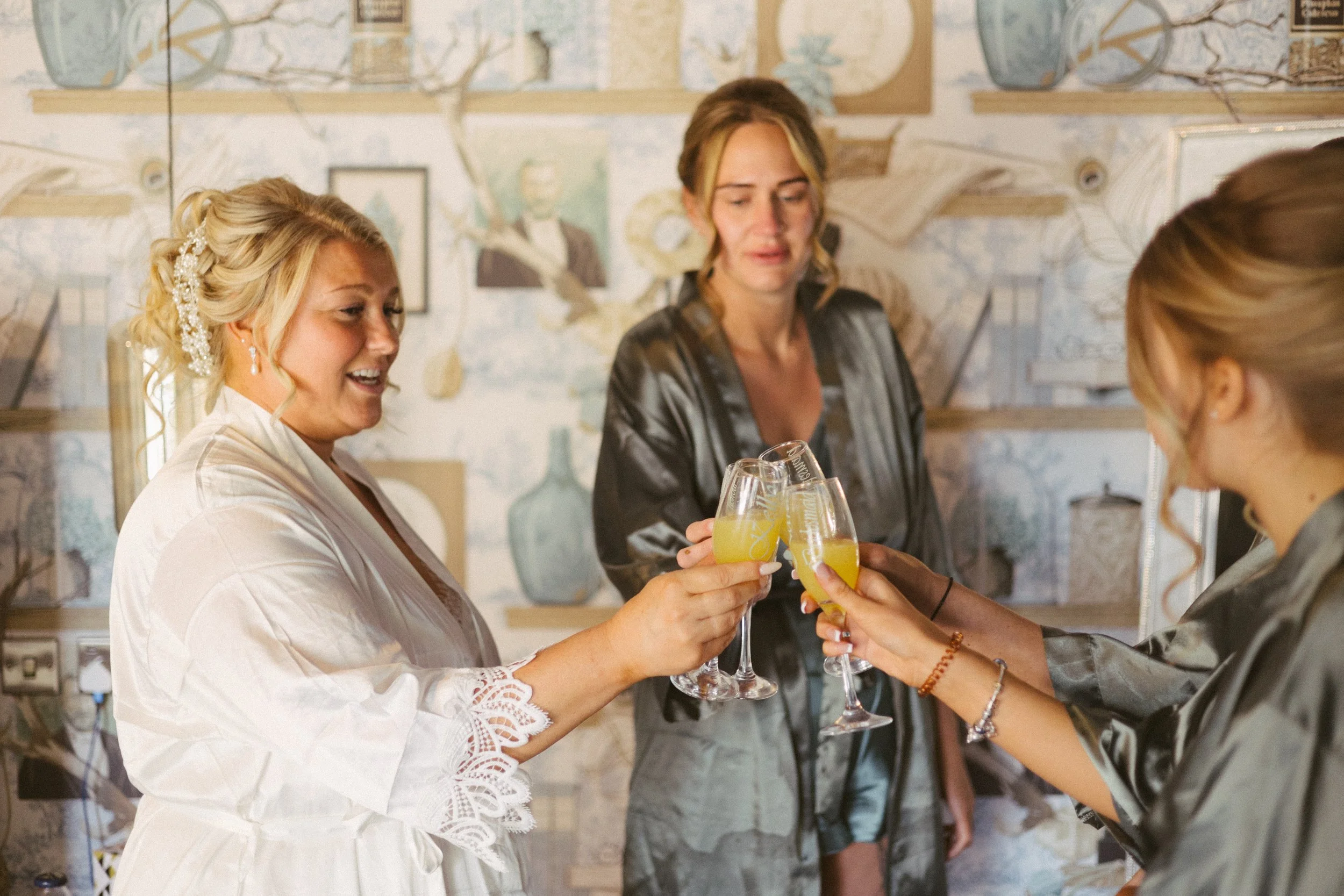 Two women in a celebratory toast with yellow drinks, smiling and exchanging glasses in a cozy interior setting.