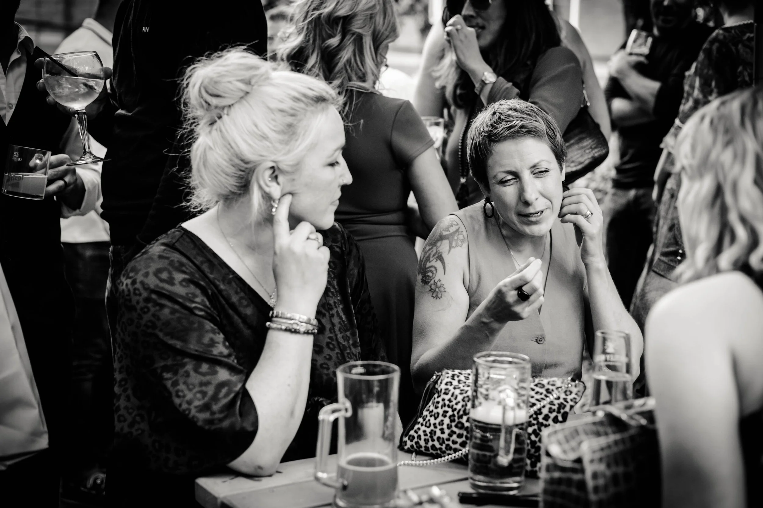 Group of women sitting at a table, engaged in conversation, with drinks on the table, in an outdoor setting.