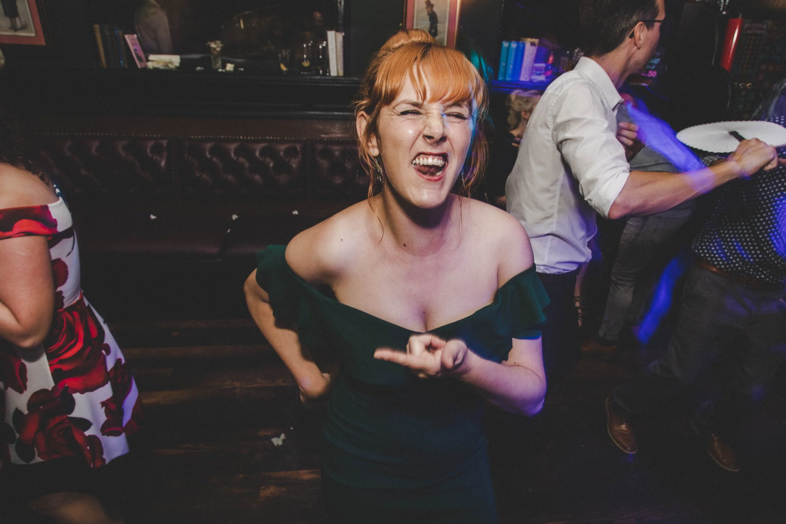 A woman with red hair smiling and making a funny face at a lively party or club, with others visible in the background.