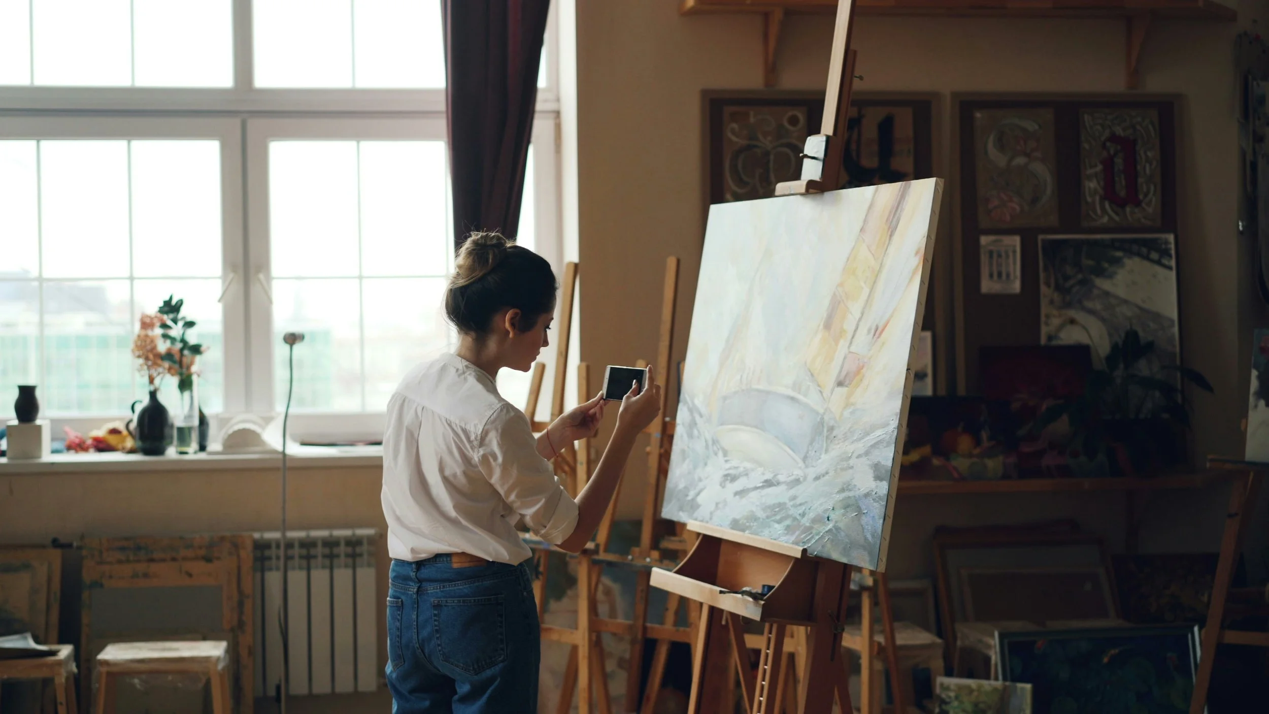A young woman in jeans taking a photo of her recently completed painting