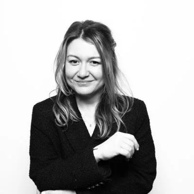 Black and white portrait of a woman with wavy hair, smiling, wearing a dark blazer, against a plain background.