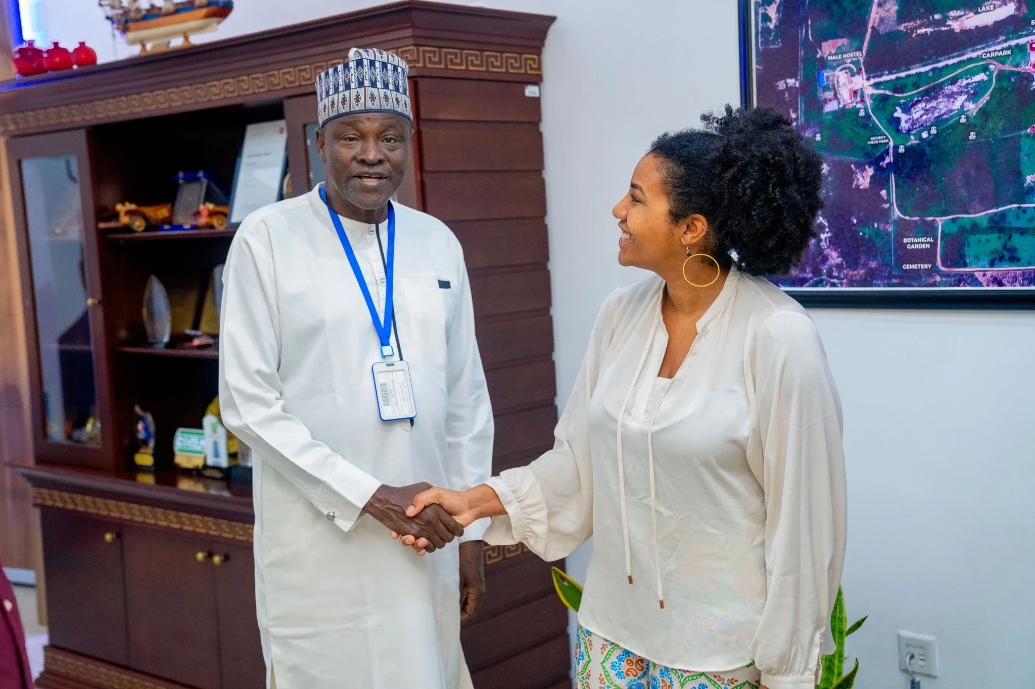 Vanessa Vovor and the Vice-Rector of Nile University of Nigeria shaking hands inside an office, with a wooden cabinet and a colorful map on the wall behind them.